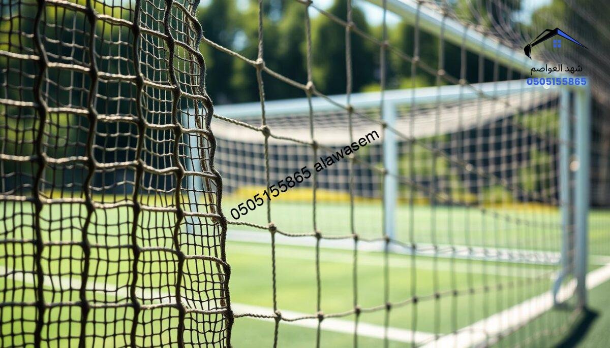 A detailed depiction of sports field nets, capturing the structure and materials used in their construction. In the foreground, focus on a section of a netting fabric, showcasing the intricate weave and sturdy texture, illuminated by soft daylight. In the middle ground, include various types of nets, such as soccer and tennis nets, hanging on a steel frame. The background should feature a blurred sports field with goal posts and a lush green surface. Use natural lighting to create a fresh and dynamic mood, emphasizing the durability of the materials. The angle should be slightly elevated, providing an overview that accentuates the complexity of the net's design and its integration into the sports environment.
